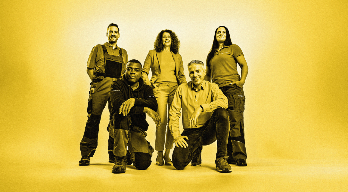 Eine Gruppe von Vonovia Mitarbeitenden vor einem gelben Hintergrund.