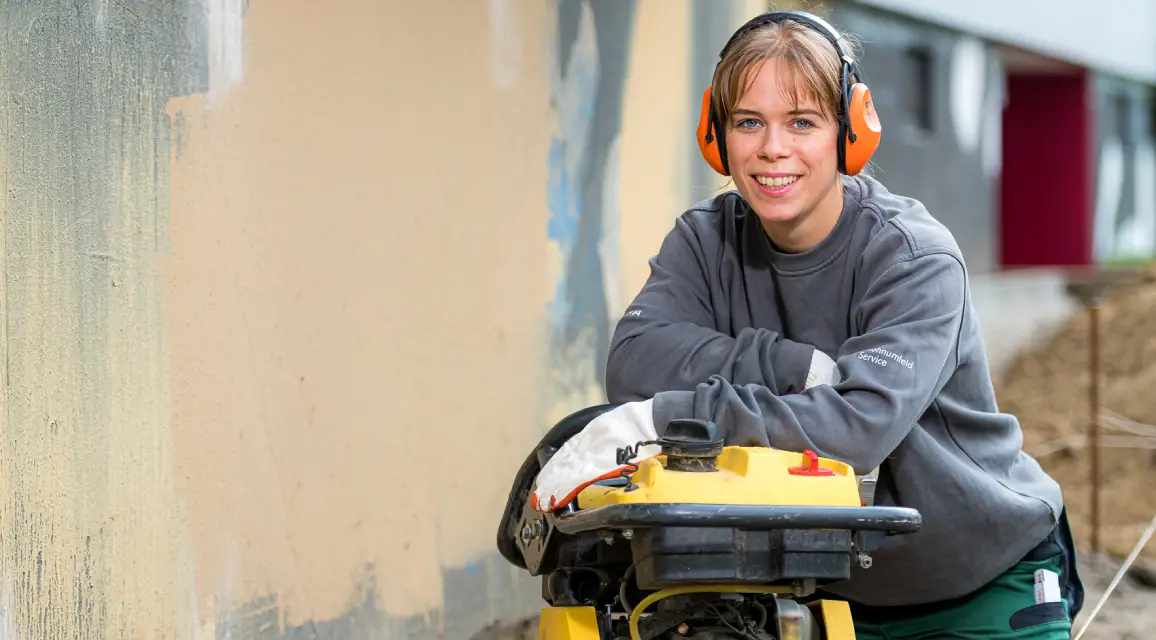 Eine Handwerkerin mit Gehörschutz lehnt auf einem Arbeitsgerät.