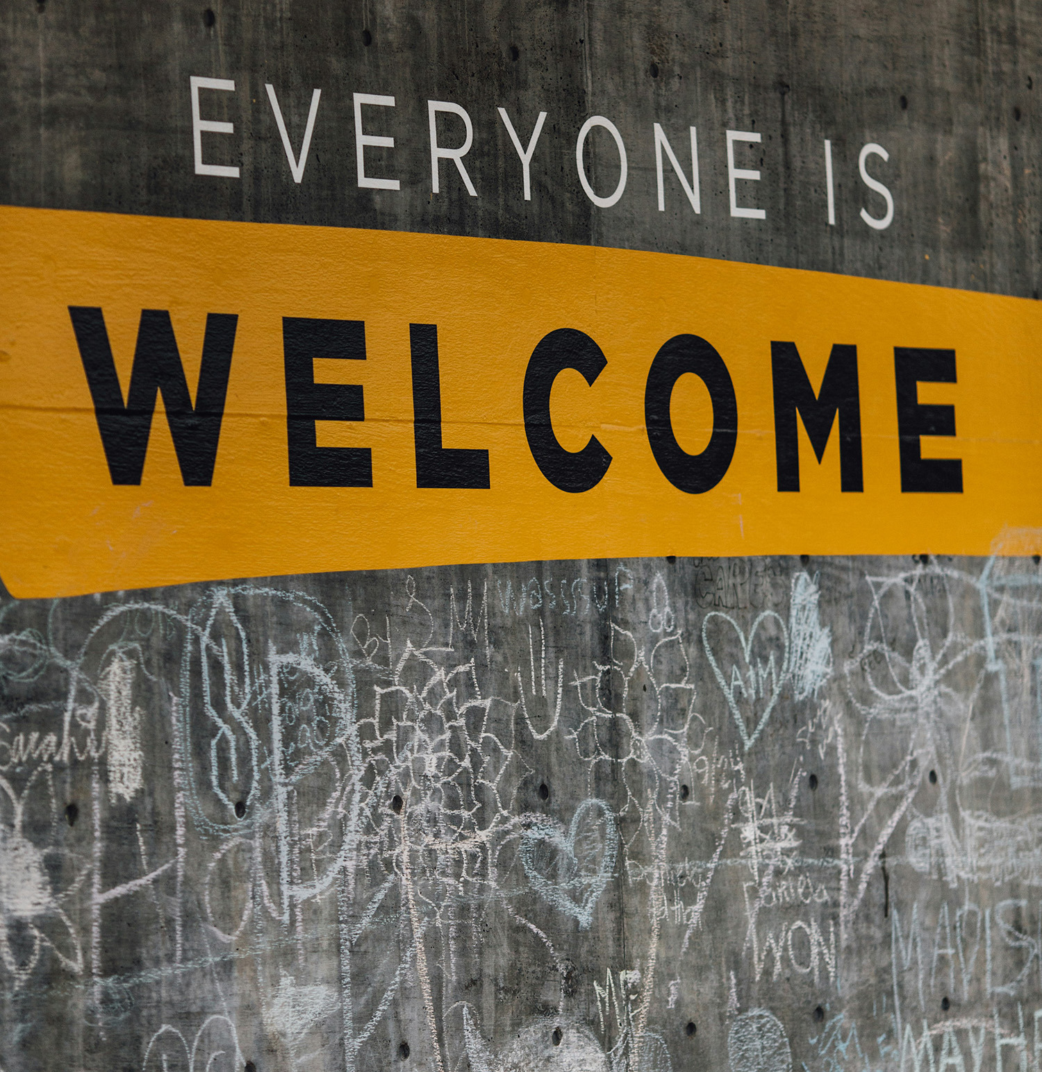 Text auf Betonwand: EVERYONE IS WELCOME, Kreidezeichnungen darunter.