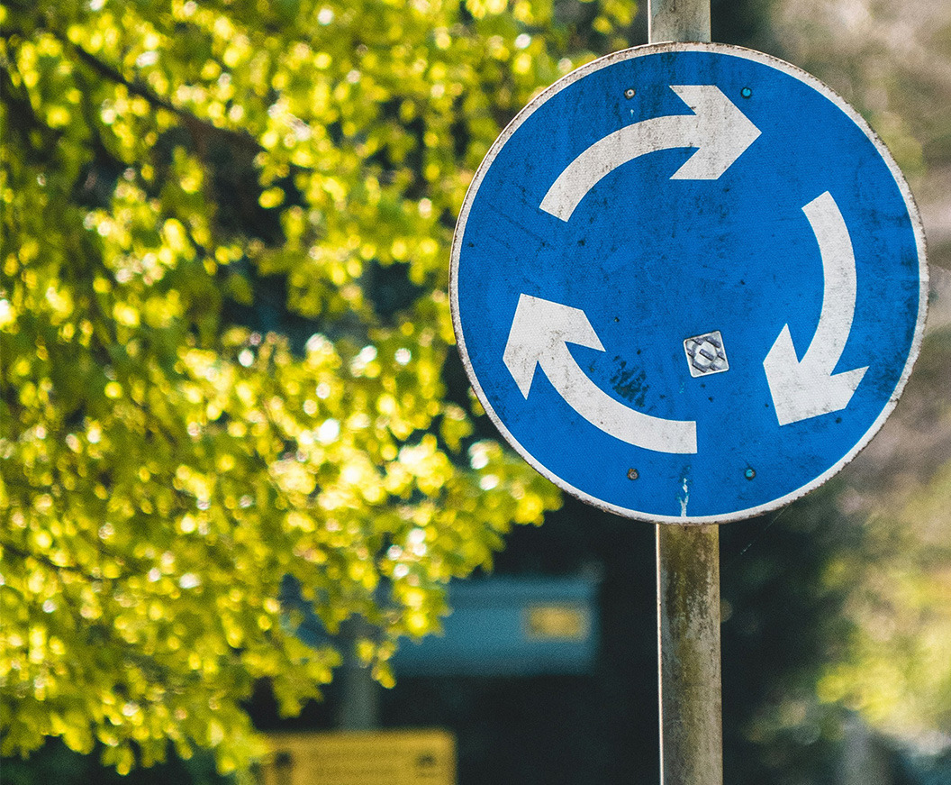 Verkehrsschild zeigt Kreisverkehr vor grünem Hintergrund.