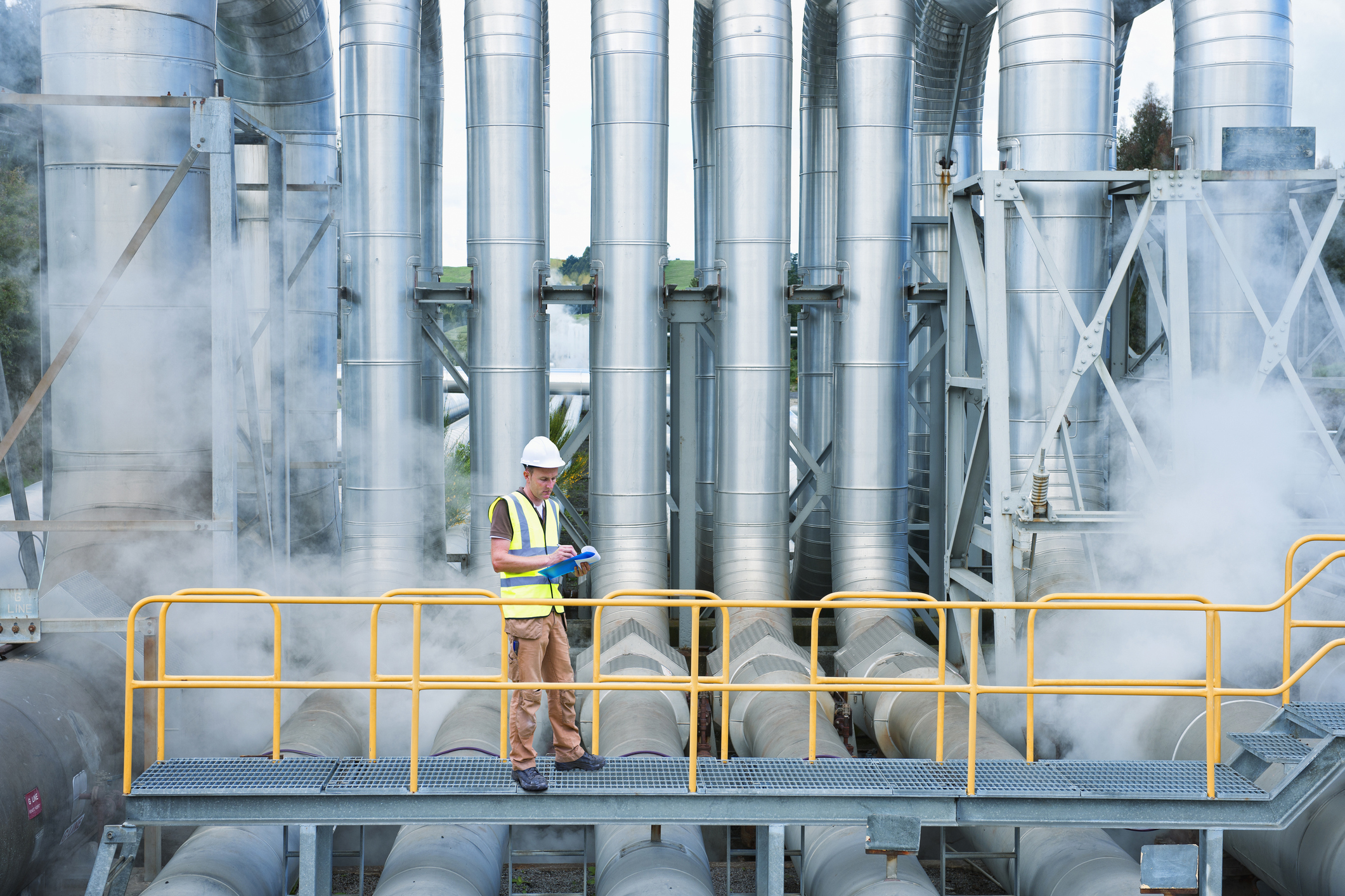 Mann in Warnweste und Helm steht vor einer Fabrik. Mann in Warnweste und Helm steht vor einer Fabrik.