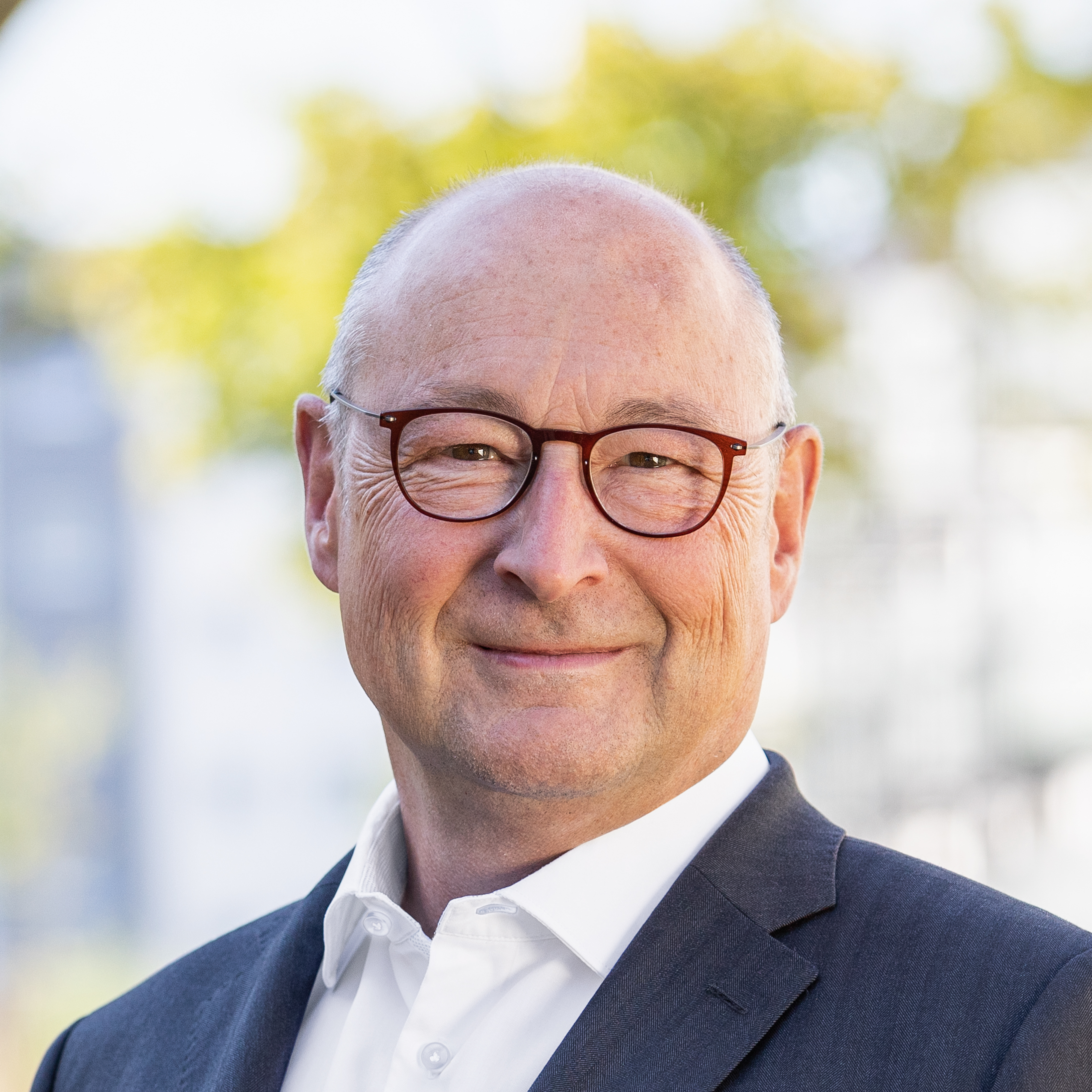 Rolf Buch im Portrait. Mann mit Brille lächelt vor unscharfem, grünem Hintergrund.