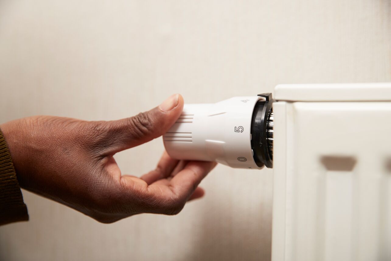 Eine Hand dreht an einem Thermostat einer Heizung.