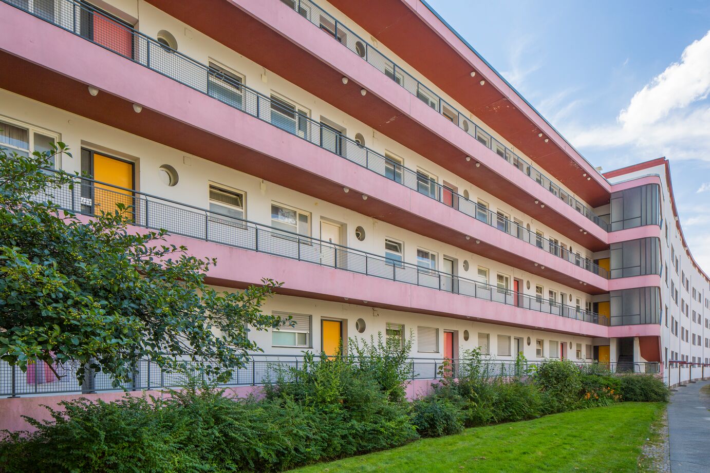 Wohnhausfassade mit Balkonen und grünen Büschen im Vorgarten.