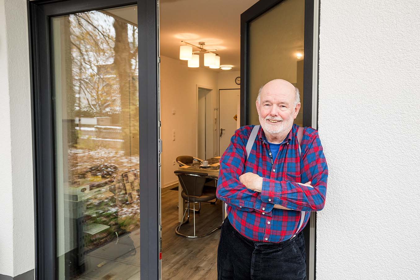 Mann - lächelnd - steht an der offenen Tür eines Hauses.