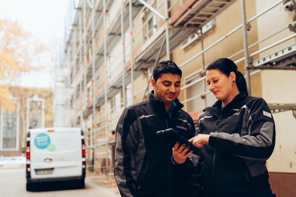 Zwei Personen nutzen Tablet, stehen neben Baustelle, Baugerüst.