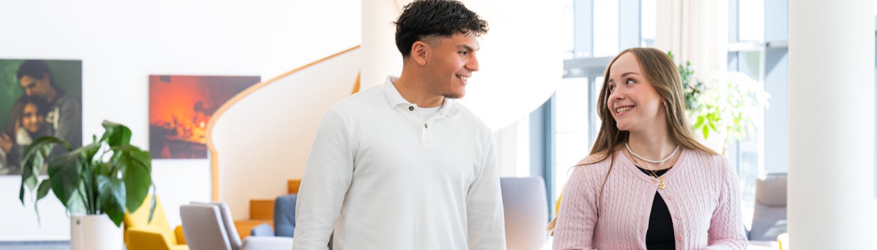 Zwei Auszubildende gehen durch ein Büro und lächeln sich an.