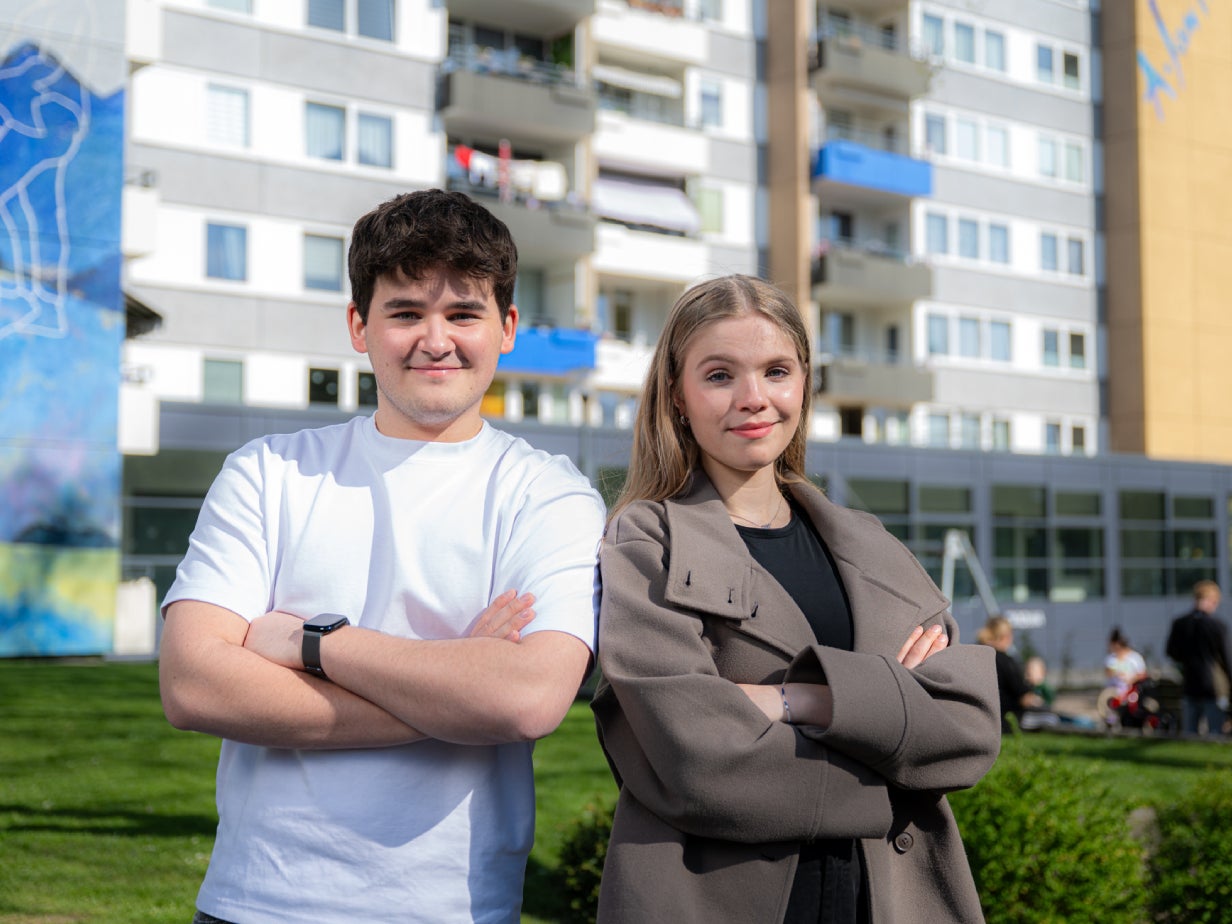 Zwei lächelnde Auszubildende stehen mit verschränkten Armen vor einem Vonovia Wohnhaus.