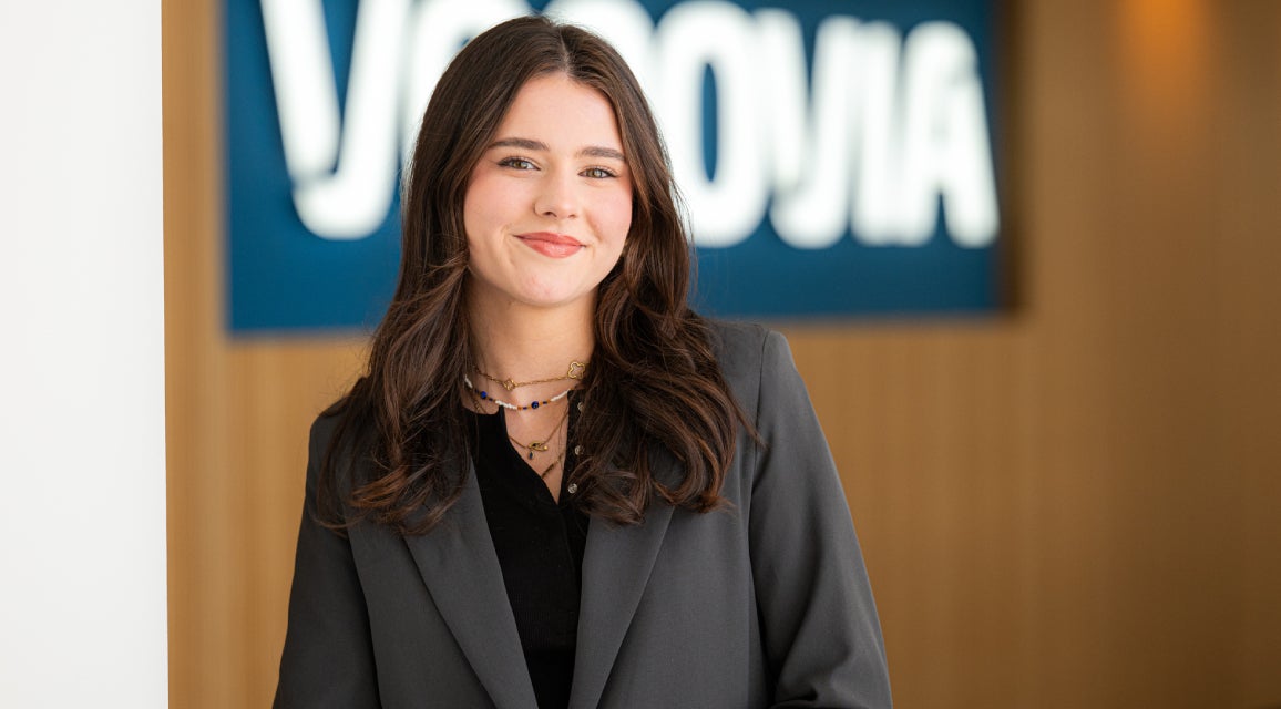 Eine Auszubildende steht lächelnd vor einem Vonovia Schild.