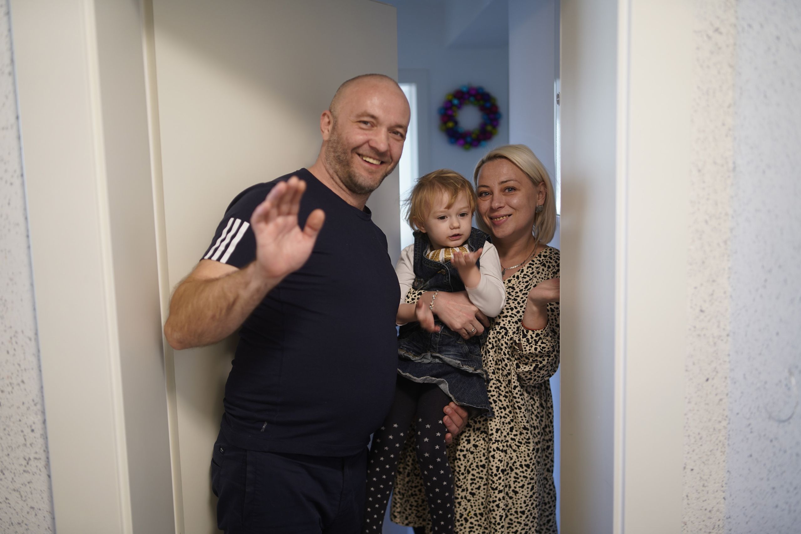 Familie mit kleinem Kind winkt und lächelt in Türöffnung.