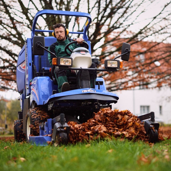 Ein Auszubildender zum Gärtner im Landschaftsbau sitzt auf einer Laubkehrmaschine.