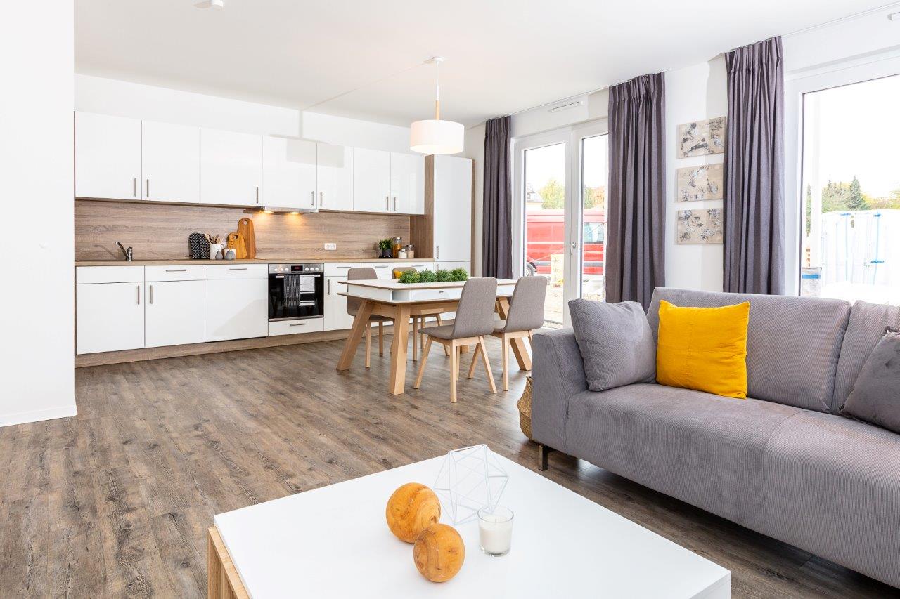 Wohnzimmer und Küche; Sofa mit gelbem Kissen; Essbereich dahinter.