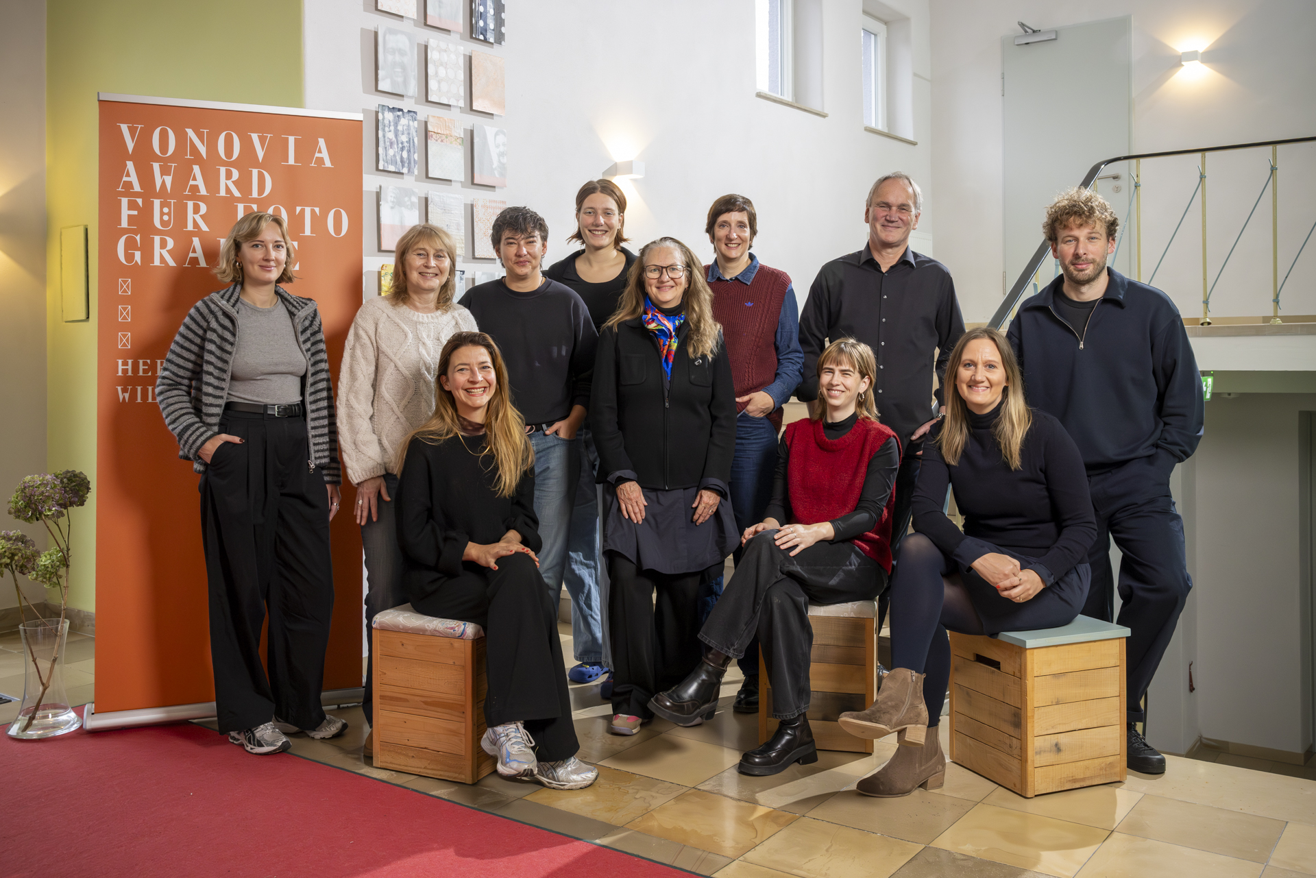 Eine Gruppe von 11 Personen steht und sitzt in einem Innenraum vor einem Banner für den Vonovia Award für Fotografie.