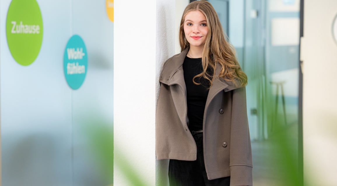 Azubi in der Ausbildung für Immobilienkaufleute steht lächelnd in einem Büro.