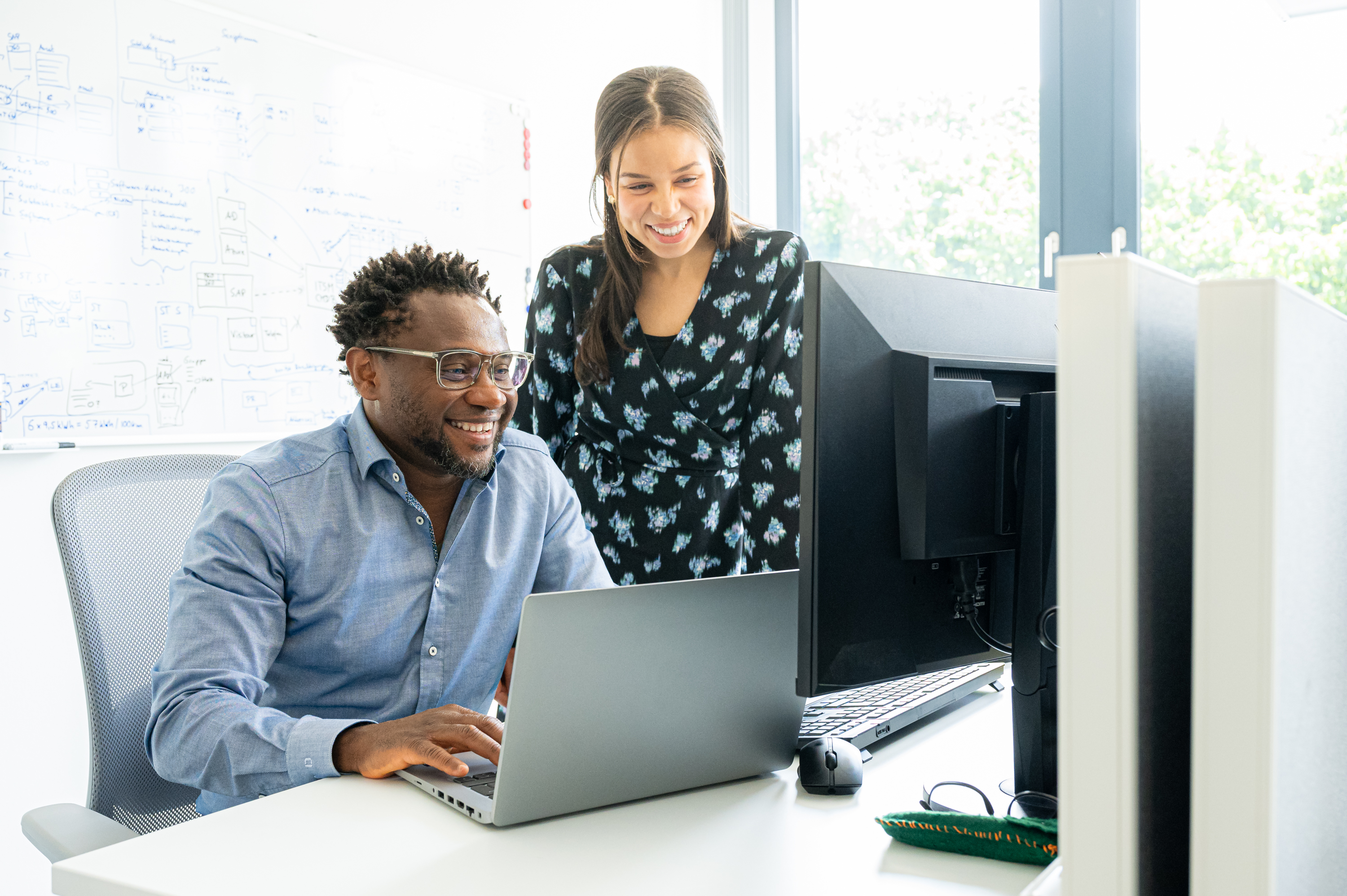 Zwei Personen, lächeln, arbeiten im modernen Büro am Laptop.