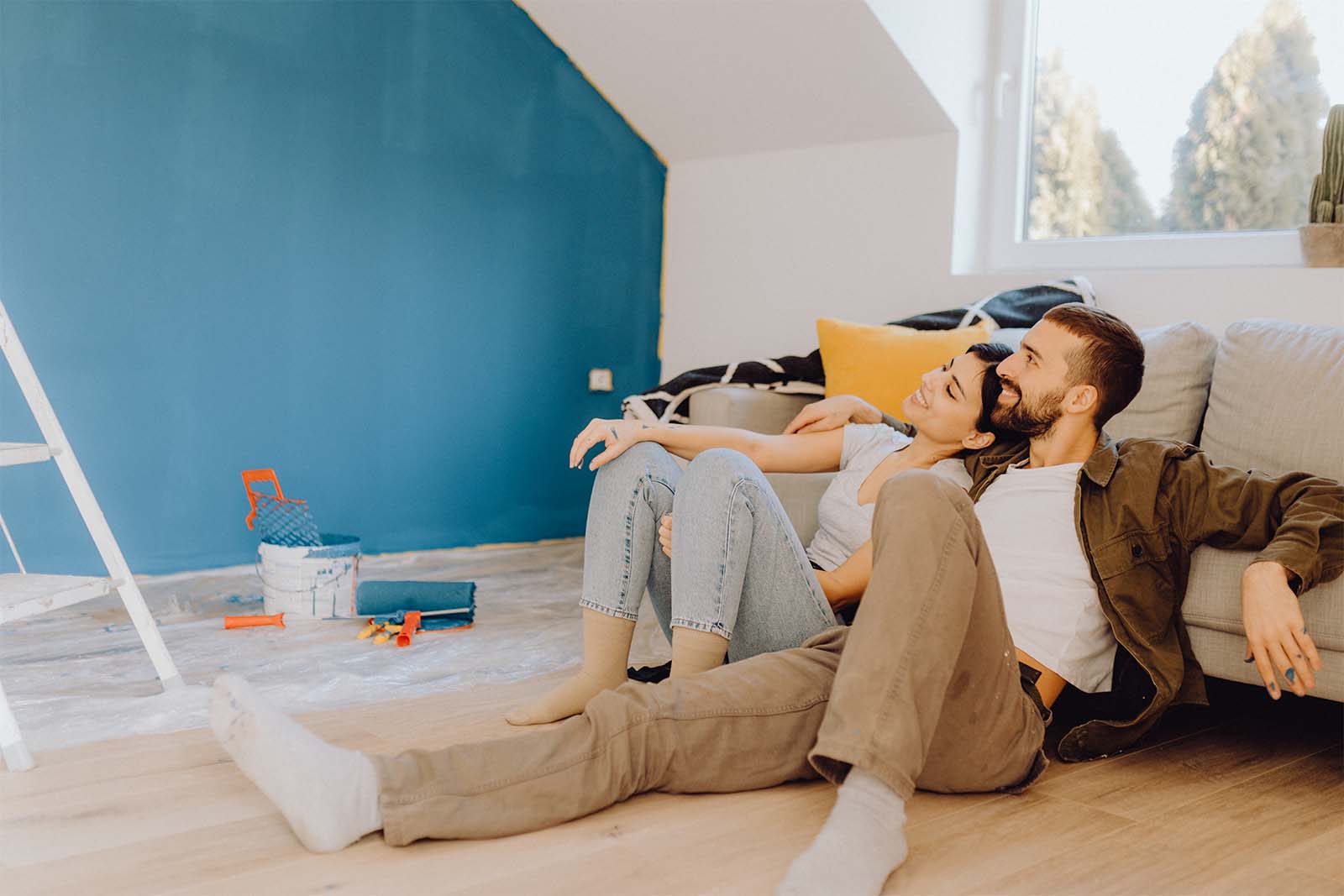 Junges Paar lehnt an eine Couch und freut sich über ihre frisch gestrichene blaue Wand.