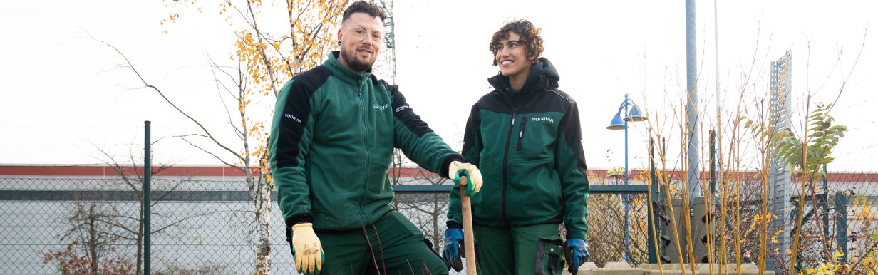 Zwei Auszubildende zum Gärtner:in im Landschaftsbau in Arbeitskleidung bei der Arbeit.
