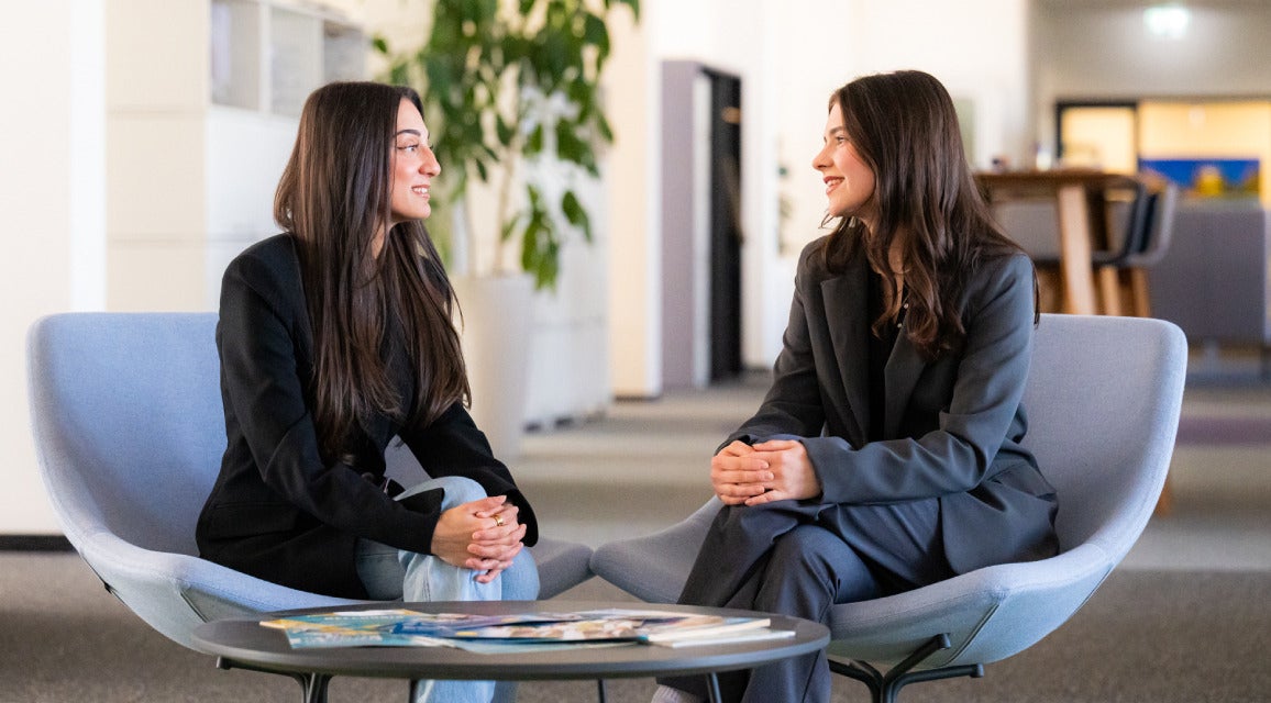 Zwei Auszubildende sitzen auf Sesseln und lächeln sich an.