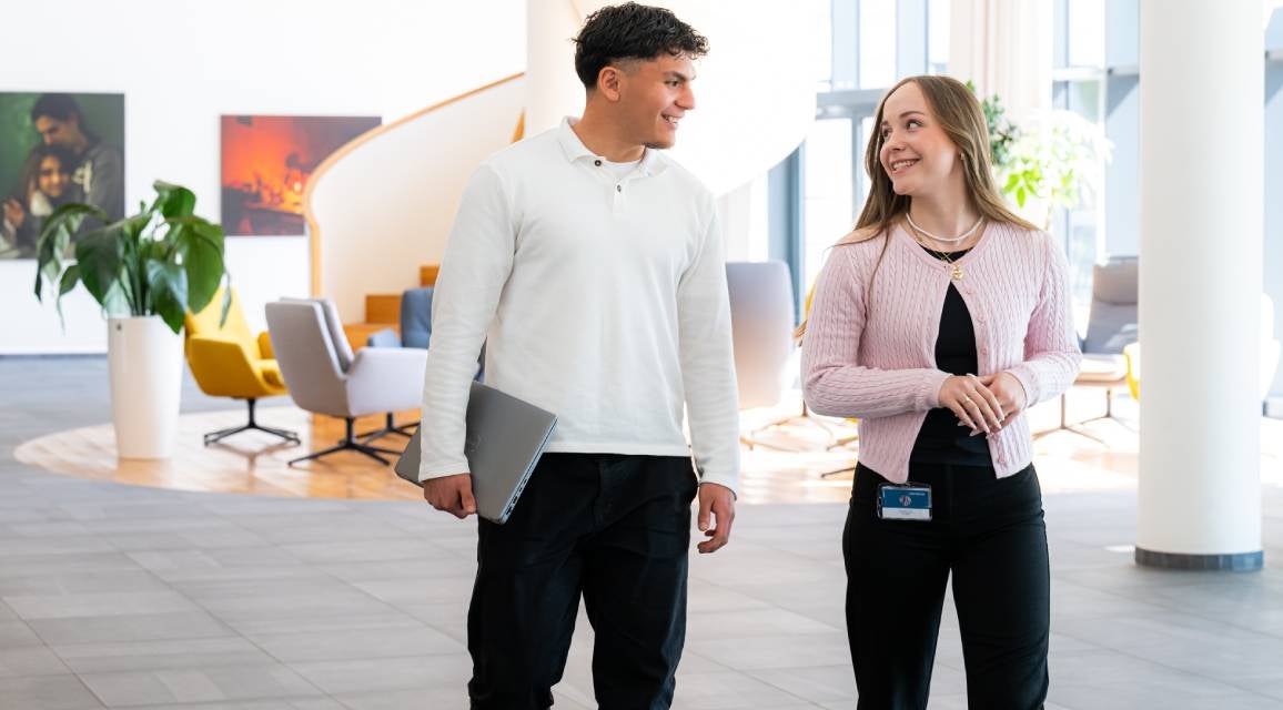 Zwei Auszubildende im Dualen Studium gehen durch das Vonovia Bürogebäude und lächeln sich an.