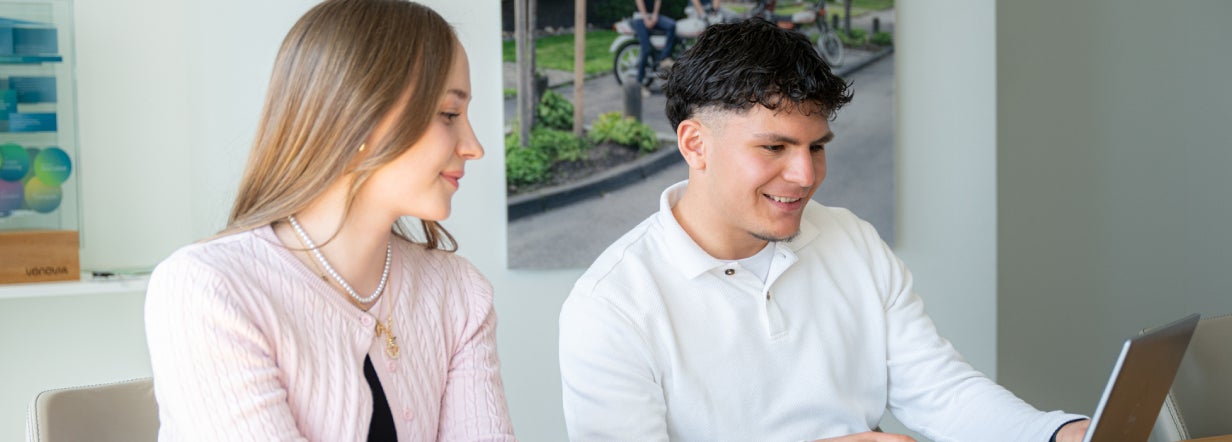 Zwei Auszubildende im Dualen Studium schauen gemeinsam auf ein Notebook.