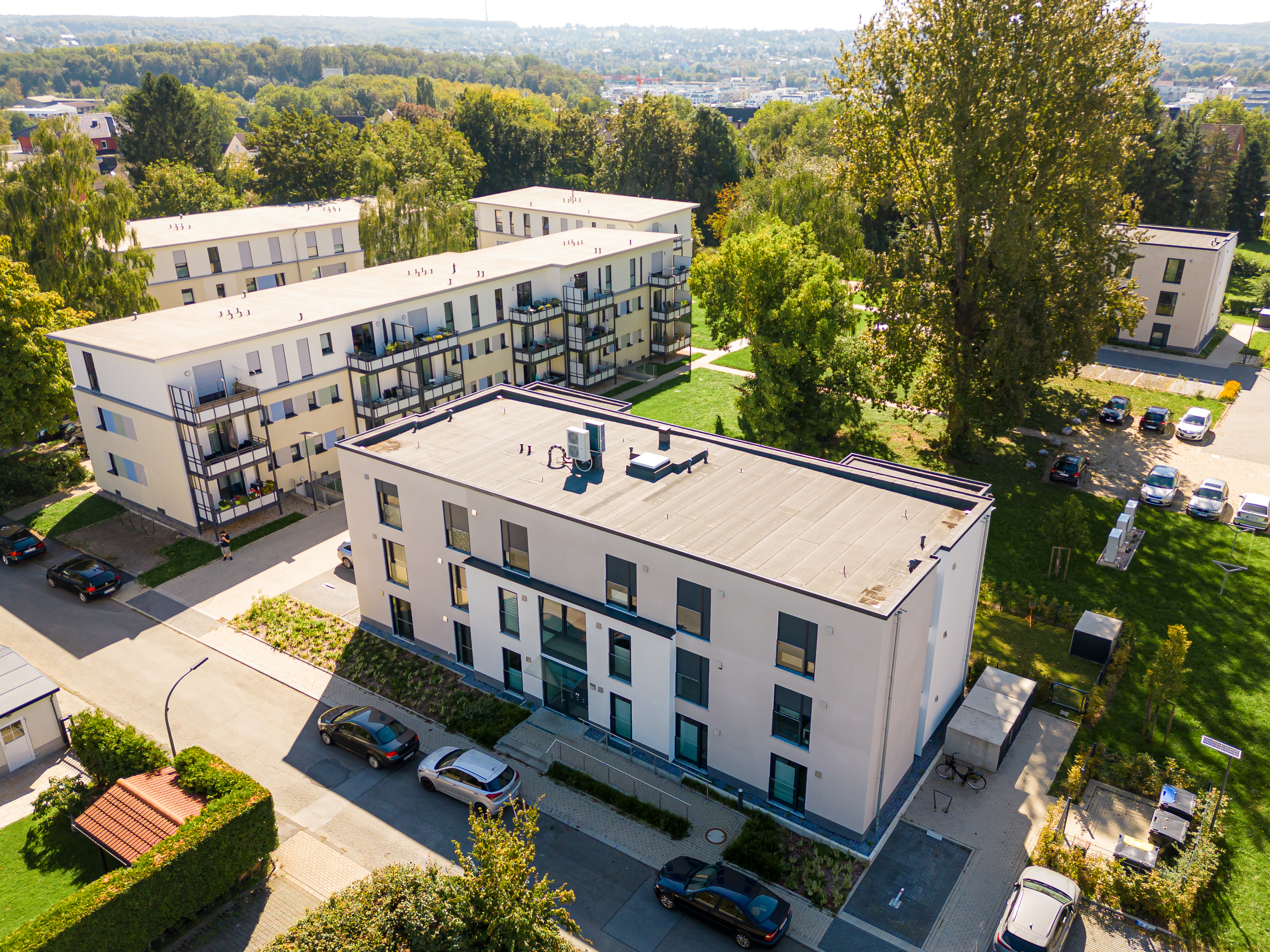 Mehrstöckige Gebäude stehen in einem grünen, bewaldeten Stadtgebiet.