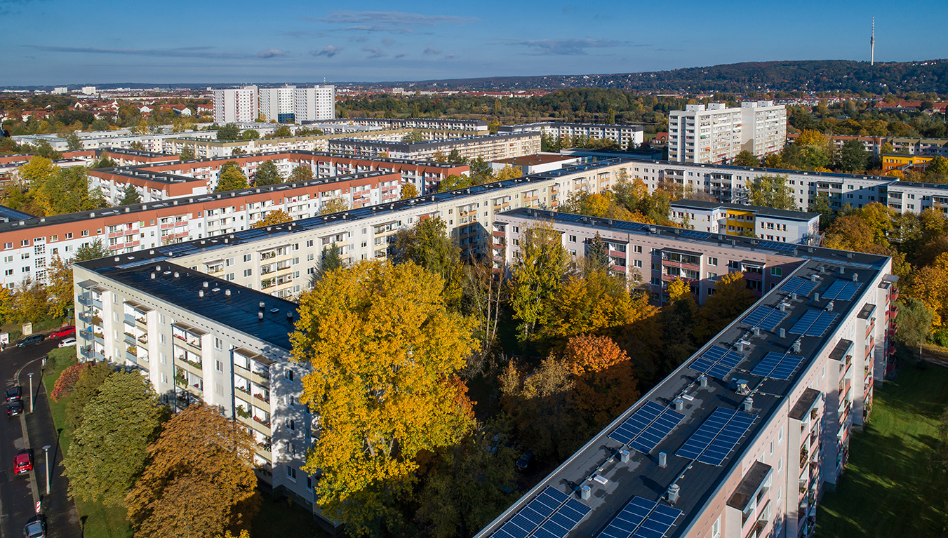 Wohnblocks im Herbst, teils Solardächer, umgeben von Bäumen.