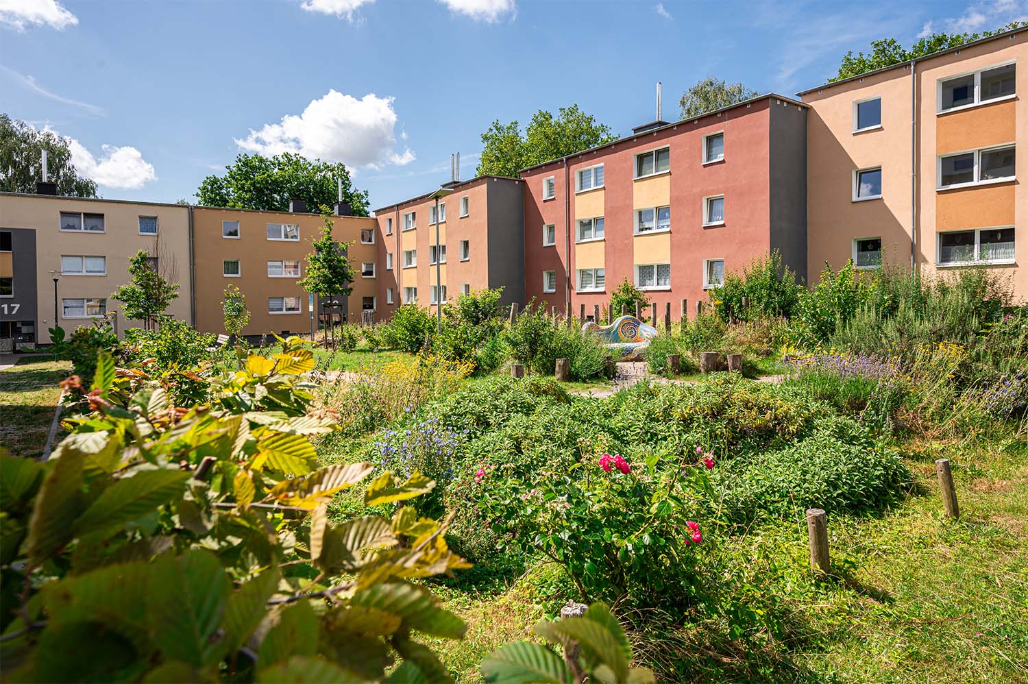 Mehrfamilienhäuser umgeben Garten mit Büschen und Blumen.