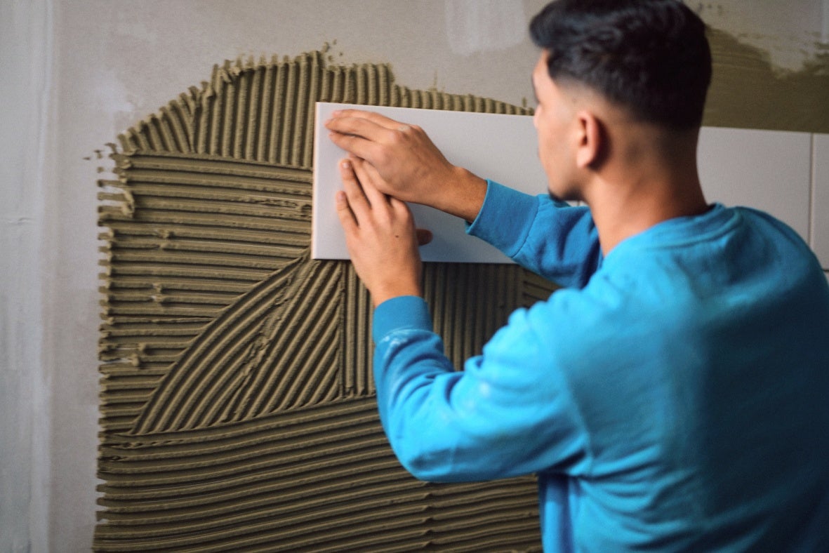 Ein Auszubildender legt eine Fliese an einer Wand.