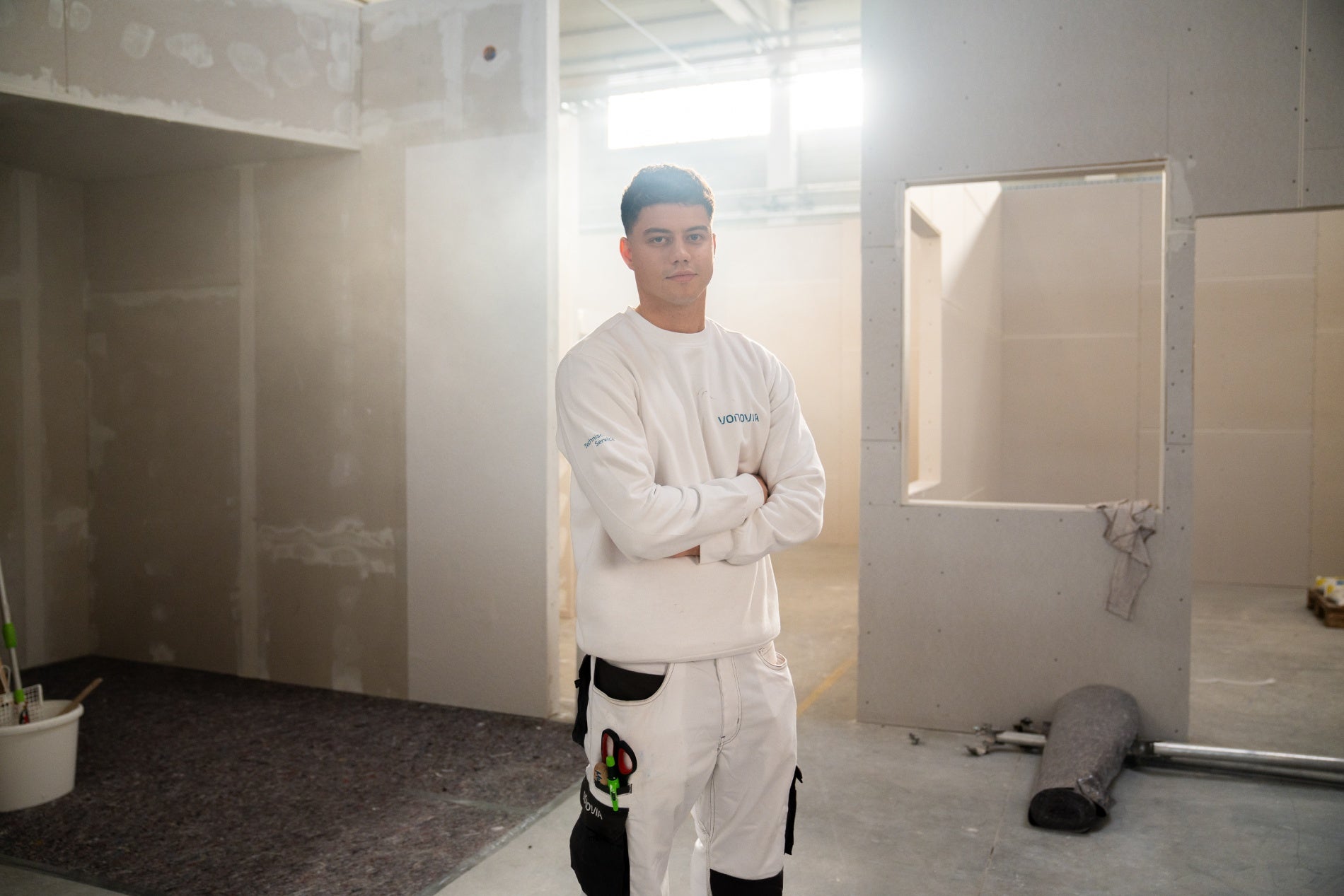 Azubi steht mit überkreuzten Armen im Innenbereich einer Wohungsbaustelle.