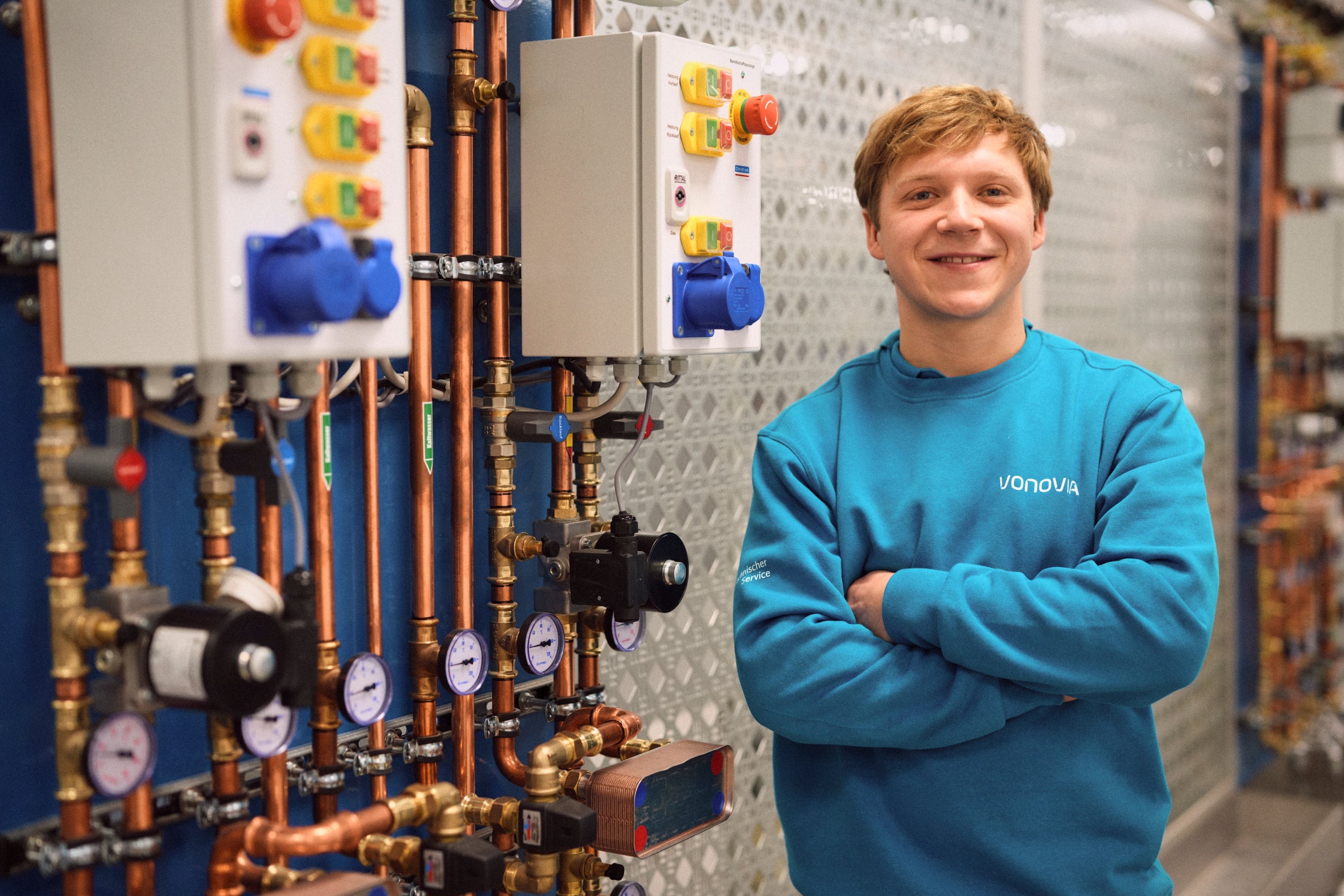 Ein Auszubildender mit verschränkten Armen steht lächelnd vor einer Anlage.