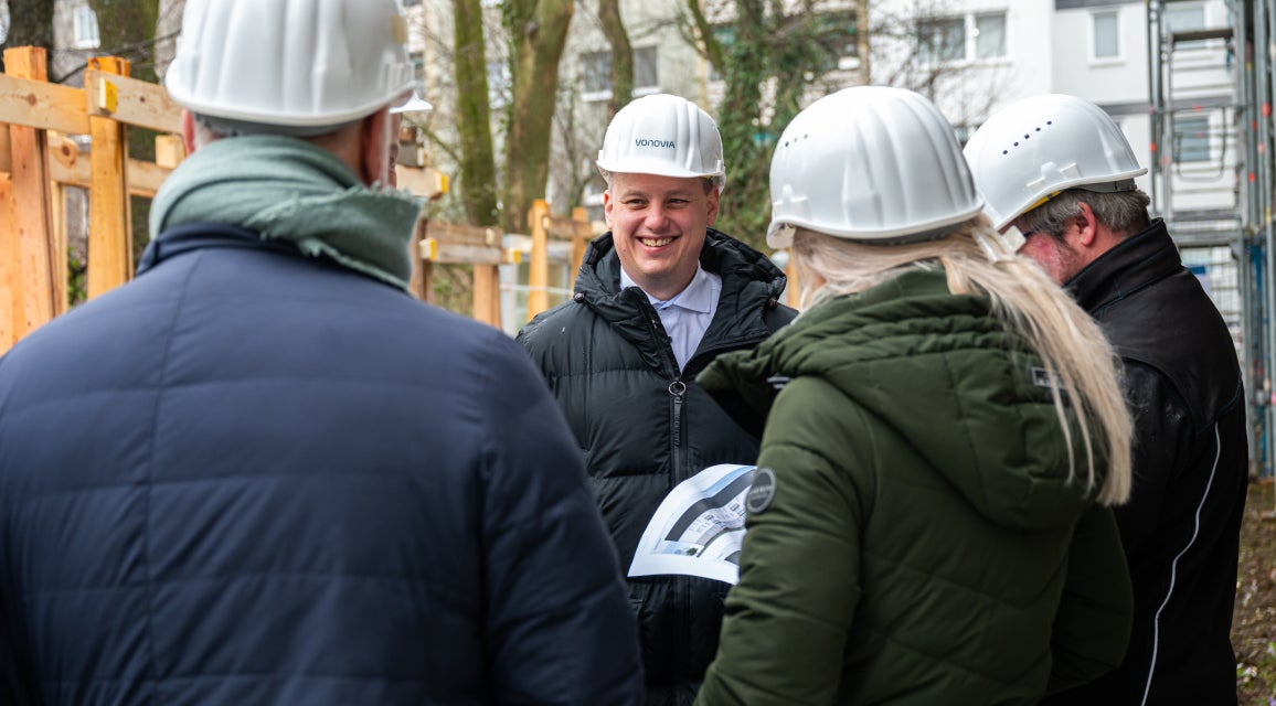 Personen mit Schutzhelmen bei einer Besprechung auf einer Baustelle.
