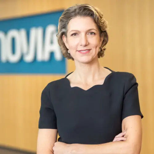 Portrait Ruth Werhahn. Frau in schwarzem Oberteil steht, Holzvertäfelung und Vonovia Schild im Hintergrund.
