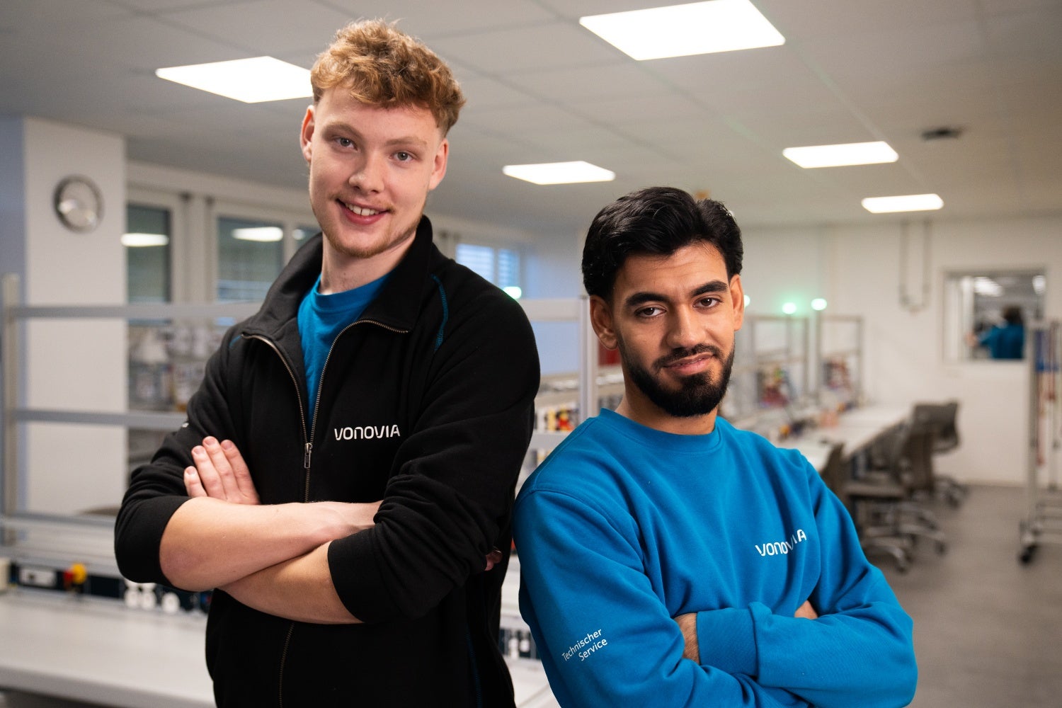 Zwei Auszubildende stehen mit verschränkten Armen und lächeln in die Kamera.