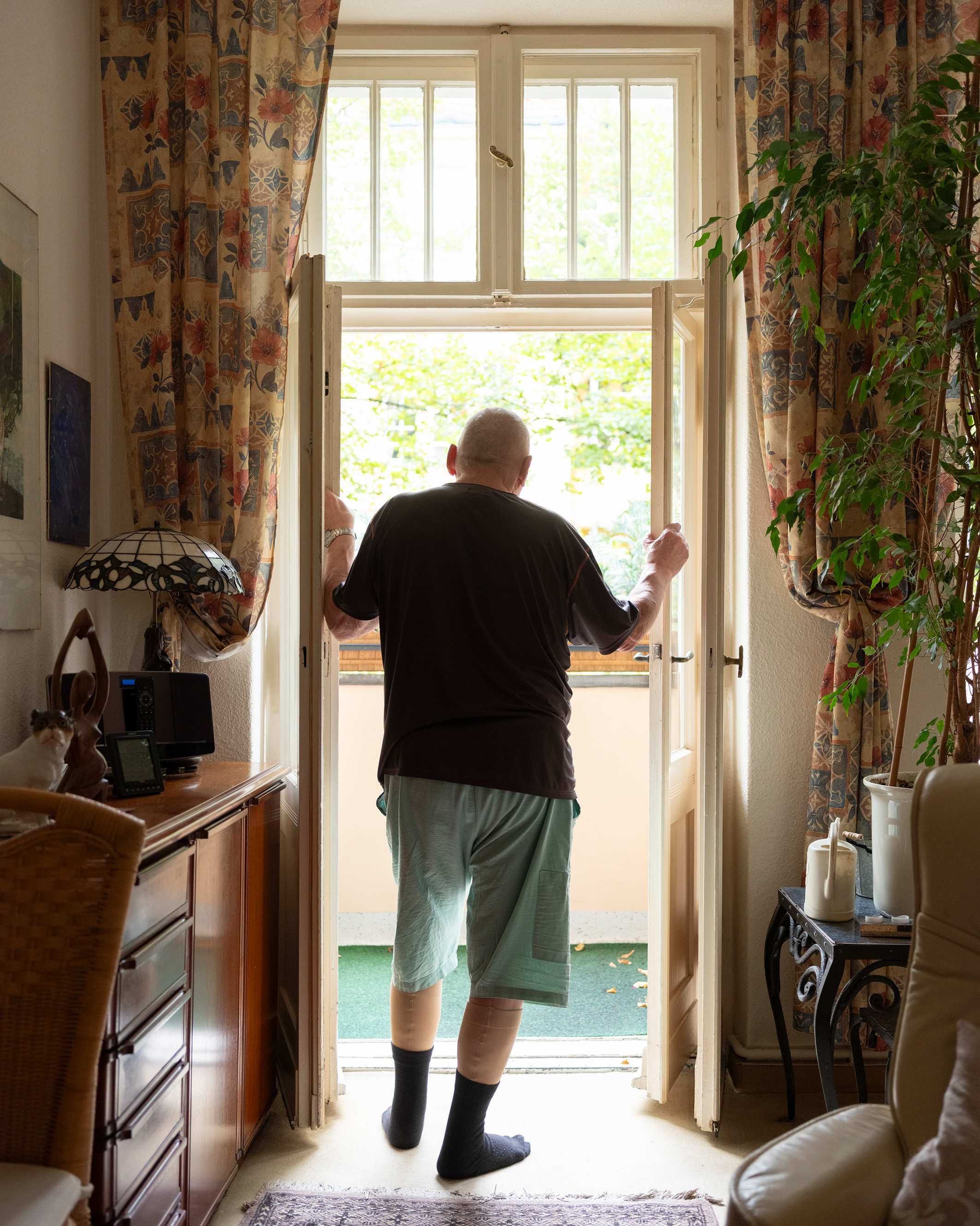 Mann, von hinten fotografiert, steht in Türrahmen zum Balkon und schaut heraus.