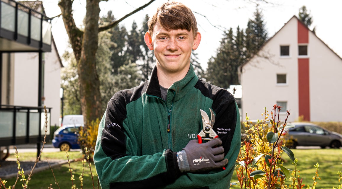 Ein Auszubildener zum Gärtner im Landschaftsbau in Arbeitskleidung mit Gartenschere in der Hand.