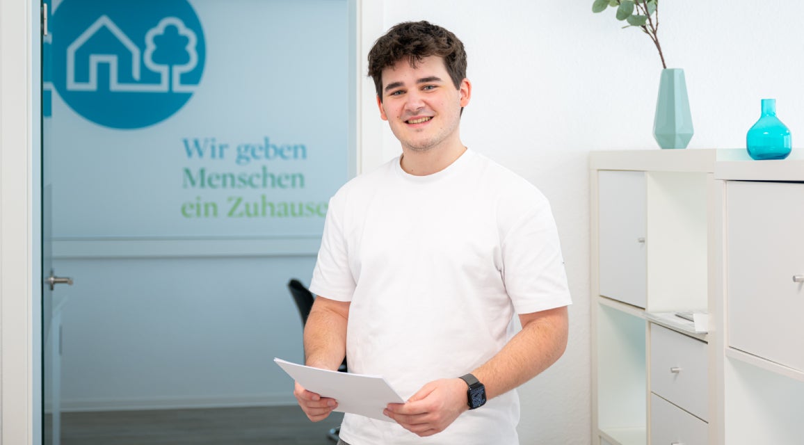 Ein Auszubildender steht in einem Büro und hält Zettel in der Hand.